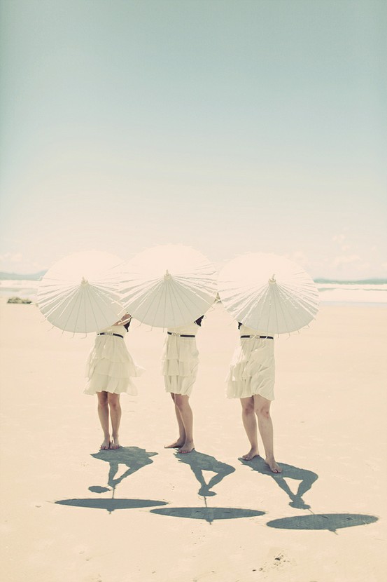 Pretty bridemaids having fun posing with white parasols on the beach